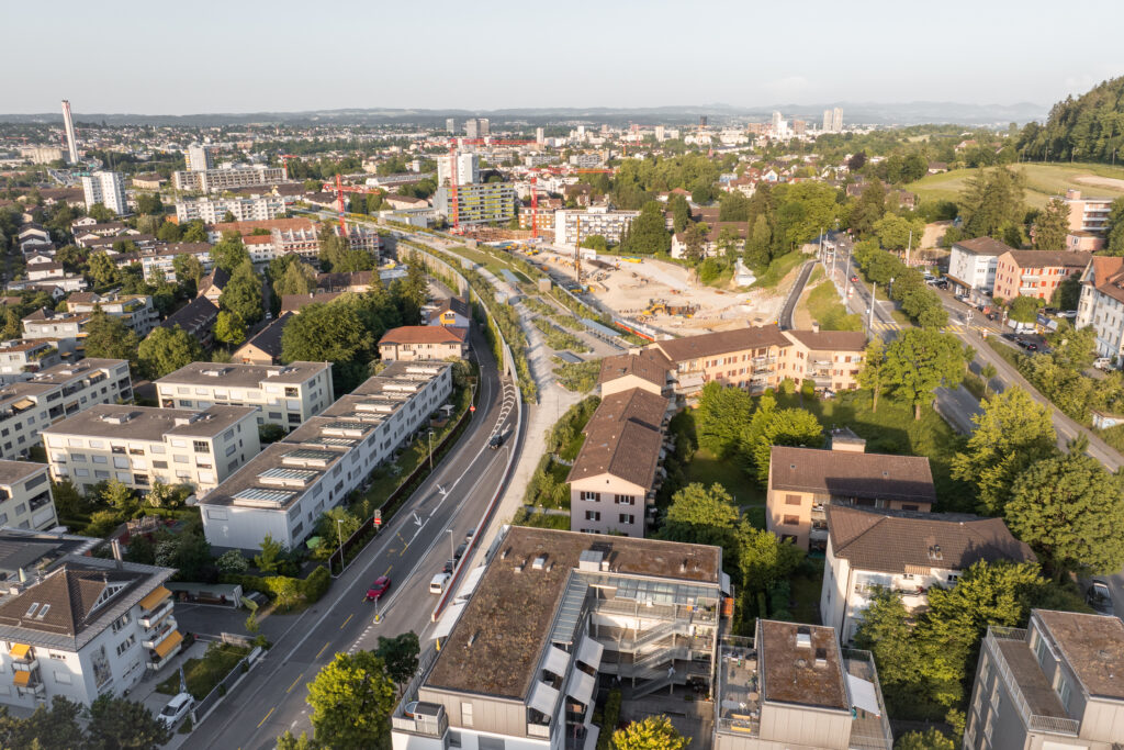 dicht bebaute Stadt, sichtbar sind auch Baukräne und eine grosse Baustelle, dazwischen einzelne Bäume. Ueberlandpark, Binding Preis für Biodiversität 2026